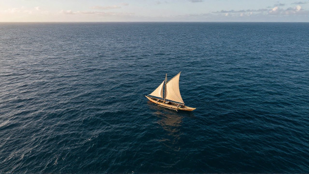 Vista aérea de una pequeña canoa de madera con velas navegando en la inmensidad del océano.